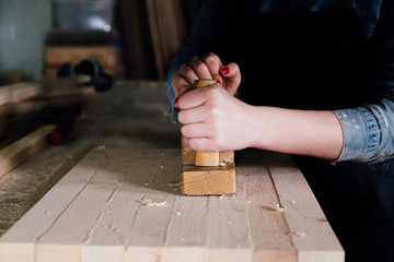 Closeup woman hands of carpenter using plane with wooden plank in carpentry workshop.