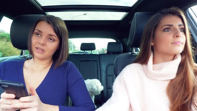 Two happy beautiful women driving car laughing looking message on smartphone