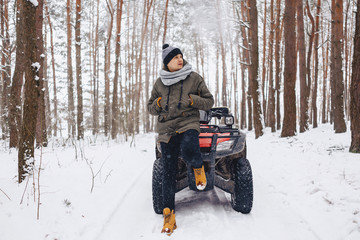 A boy is standing near a quad bike in the middle of the forest