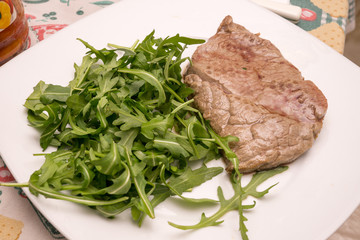 beef steak with rocket garnish, on white plate