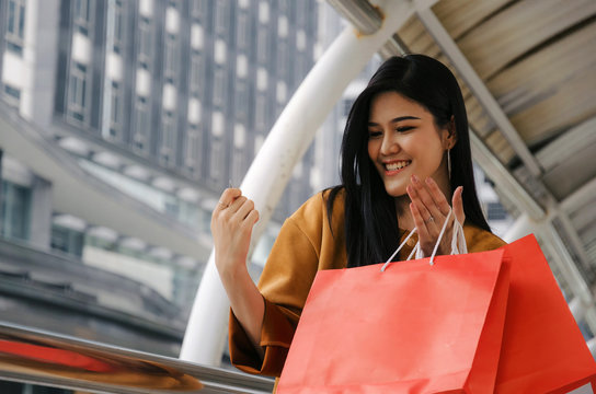 beautiful cheerful asian holding many colorful red shopping bags and credit card walking in modern big city, fashion, promotion, special offer, winter sale, people, payment and shopping online concept