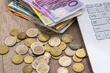 euro bills and coin with laptop on desk