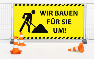 Gruppe von Pylone Pylonen Verkehrshütchen Leitkegeln vor Mobilzaun Bauzaun mit gelben Banner und Warnmarkierung - Wir bauen für Sie um