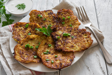 homemade potato pancakes with sour cream and fork on rustic wooden table