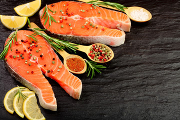 Slice of red fish salmon with lemon, rosemary on black stone background with copy space for your text. Top view