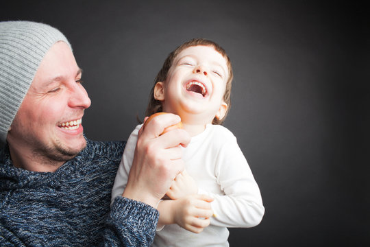 Dad plays with a lovely little son, sitting on his hands on a black background in the Studio. It amuses it with Apple and they both laugh. Photos to celebrate father's day