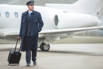 Full length portrait of calm pilot holding baggage while going to aircraft. Journey concept. Copy space © Yakobchuk Olena