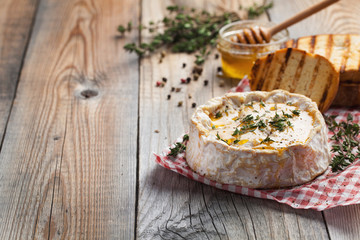 A real Camembert from France with thyme, honey and toasted bread on old wooden rustic table. Soft cheese on a wooden background with copy space