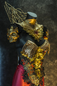 fantastic gold armor and handmade metal pieces, it has a gold dragon scaled breastplate with a helmet of gothic pieces and red feathers, it has a red skirt and metal pieces of jewelery