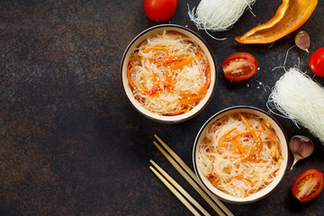 Funchoza salad with rice noodles with paprika and pepper on a dark stone or slate background, top view with copy space.