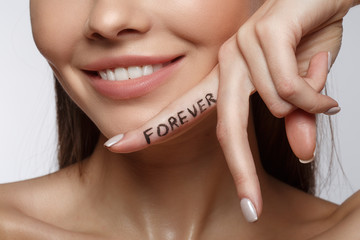 Close up of positive young woman keeping finger near her chin and smiling. Beauty forever concept