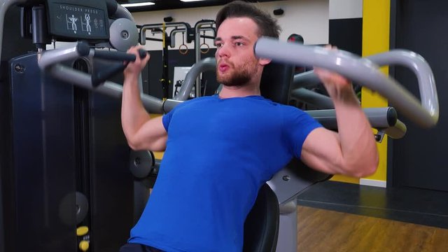 A young fit man trains on a machine in a gym