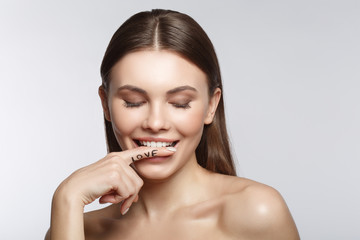 Portrait of sensual young woman keeping finger near her lips and smiling. Her eyes are closed with fondness. Isolated. Love concept