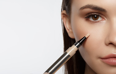 Close up of half female face. Confident young woman is applying concealer on her cheek. Isolated...