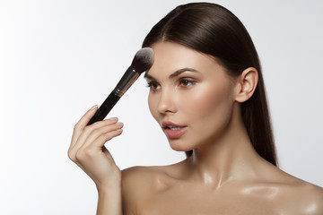 Obraz premium Serene young lady applying powder on forehead by brush with concentration. Isolated and copy space