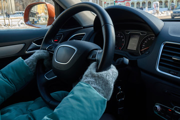 Female hands in the mittens on the steering wheel