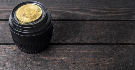 golden bitcoin lays on camera lens on wooden background