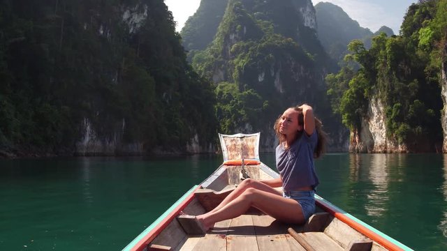 Wonder travel woman exploring wild nature of Khao Sok national park. Sitting in wood long tail boat on tropical limestone cliffs background. Lifestyle image. Island lagoon.