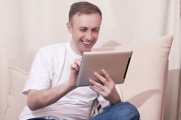 Technology Concepts. Happy Caucasian Man with Tablet Computer Chatting on Couch. Posing  in Home Environment.