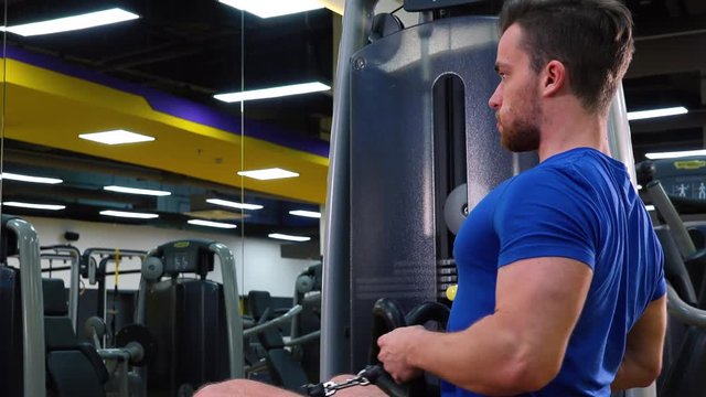 A young fit man trains on a rowing machine in a gym - closeup from the side