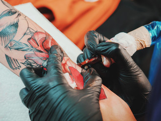 Tattoo artist at work. Woman in black latex glove tattooing a young man's hand with colorful...