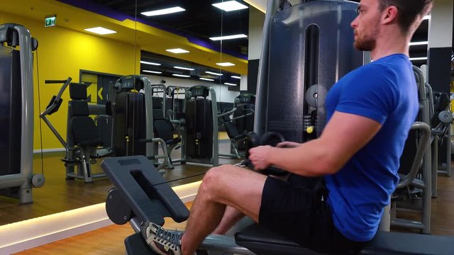 A young fit man trains on a rowing machine in a gym - view from the side