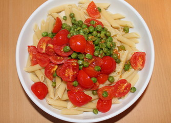 Penne pasta with cherry tomatoes and peas in a white bowl.