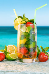 Mojito cocktail. White rum cocktail with fresh ingredients. Cold ice drink on blurred beach background.