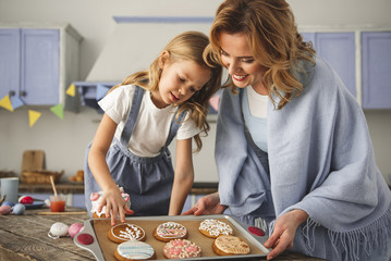 Satisfied mother and daughter standing in the kitchen and looking at cookies prepared for easter