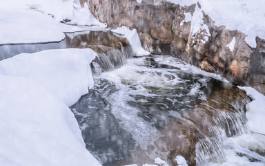 A winter scene of a waterfall surrounded by snow