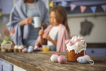 Serene mother and child colorizing eggs. Focus on traditional sweet bread standing on table