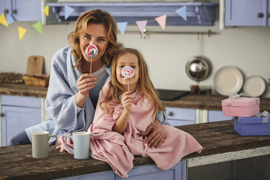 Playful mom and kid relaxing at home with comfort. They are holding candies in front of nose. Copy space in right side