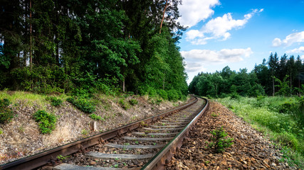 Fototapeta premium Romantic scenery with rails in summer forest. Bend of railway tracks in green nature with trees and blue sky with white clouds.