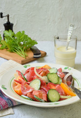 Vegetarian healthy salad with fresh ripe summer vegetables: tomato, cucumber, pepper and onion on light wooden background.