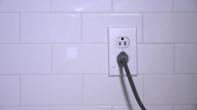 A man plugs and unplug an electrical cord into a typical kitchen outlet. Power energy savings concept.  	