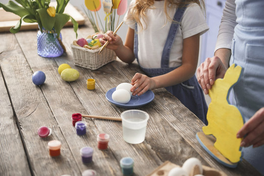 Mother and child hands making different easter decorations on wooden table. Close up