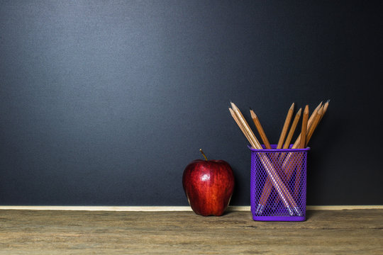 Education concept. Pencil and red apple on wood table with blackboard (chalkboard) as background with copy space.