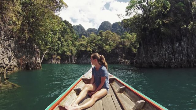 Graceful woman with long legs relaxing on boat enjoying wild nature on long tail boat trip at Khao Sok national park . Excursion in Thailand. Beautiful traveler girl on tropical vacation .