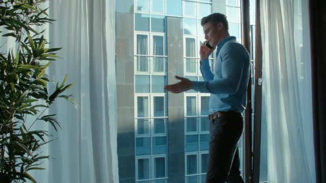 Businessman making phone call while standing near a window. Man dressed in formal standing near window of highrise office building overlooking the cityscape.