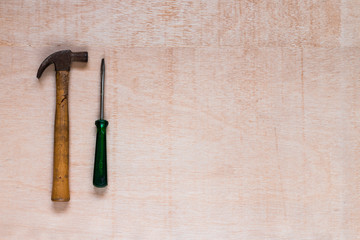A hammer and a screwdriver in the left corner of the picture on a wooden table