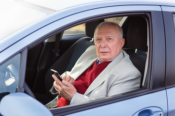 Old Senior business man driving a car and texting on a mobile phone