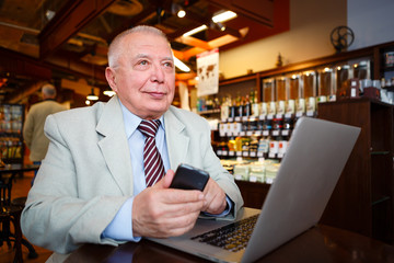 Fototapeta na wymiar Old senior businessman in suit and tie with laptop computer and smartphone, sitting in city cafe house