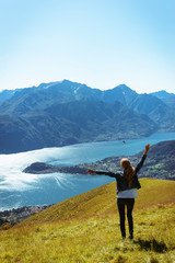 Fototapeta na wymiar Young traveling woman with raised arms in jeans high on the top of the mountain Alps on lake Como in Italy Lombardy region with long tale hair, enjoying a beautiful nature at early morning