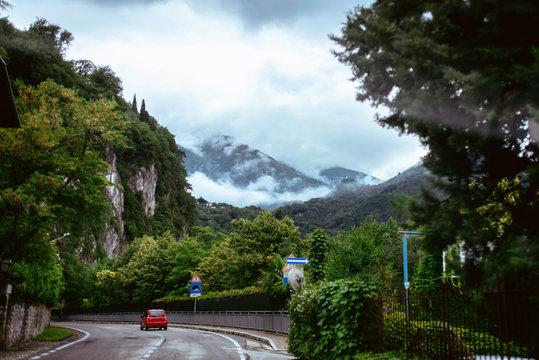 Italy Lake Como Wideangle lens shot of red italian car at mountain road with tunnel among forest at foggy rainy day of June