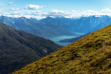 Obraz premium Panoramic View of beautiful landscape in the Italian Alps with fresh green meadows and snow-capped mountain tops in the background on a sunny day with blue sky and clouds in springtime.