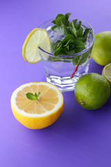 Mojito on an ultraviolet background, a cocktail with mint, lemon and lime, a soft drink for summer relaxation, a cocktail on a purple background, a pop art drink, half a lemon and lime, minimalism