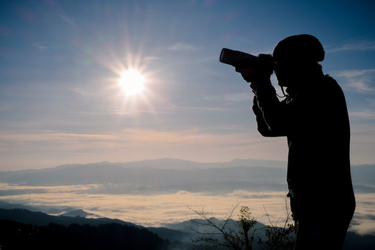 Silhouette of free and happy photographer with camera at sunset time on the mountain view. Freedom, success and triumph concept