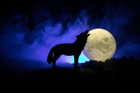 Silhouette of howling wolf against dark toned foggy background and full moon or Wolf in silhouette howling to the full moon. Halloween horror concept.