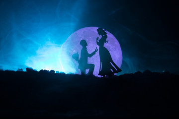 Amazing love scene. Silhouettes of man making proposal to woman or Silhouettes of couple against big moon at background
