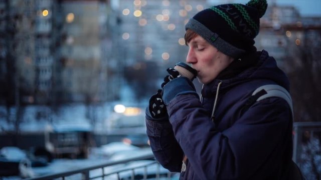 Young man drinking coffee and having cold while waiting someone outside on winter